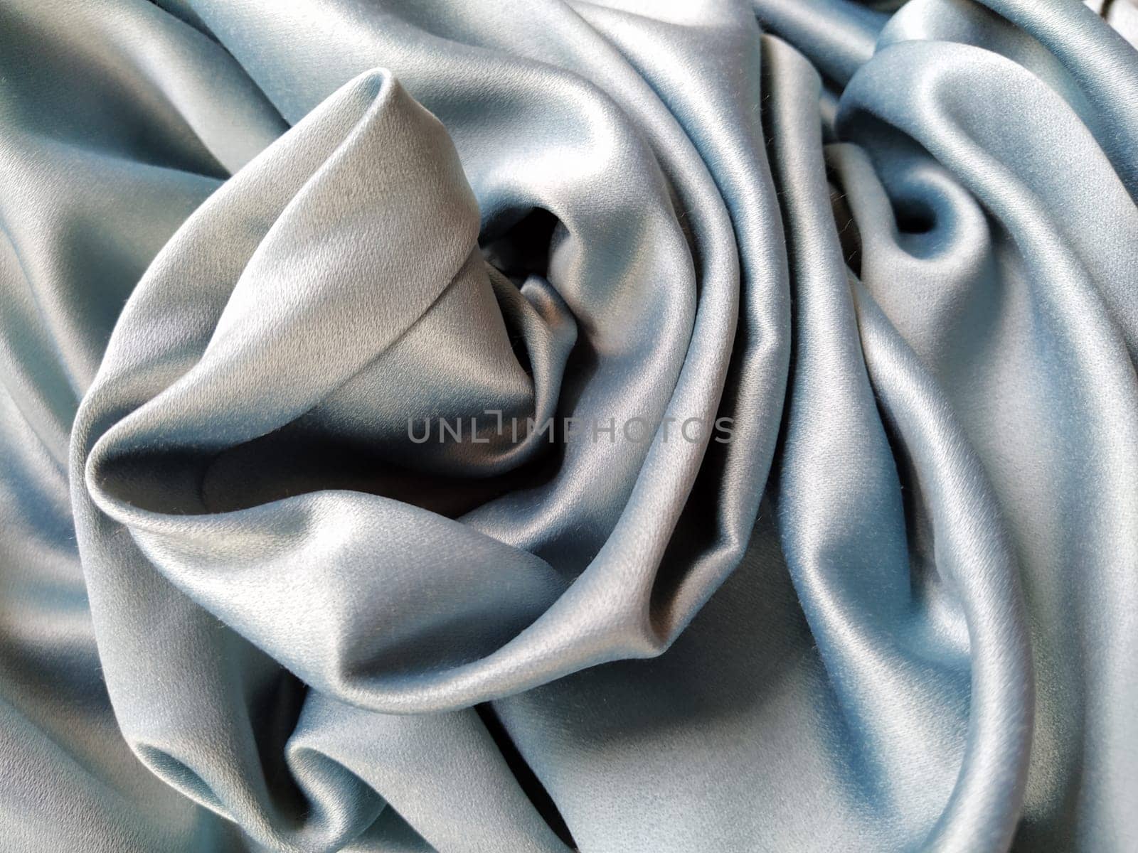 Silky to the touch fabric of gray - blue color with a brilliant shimmer. Natural lighting, light and shadow. The material is casually folded. Polyester Textile