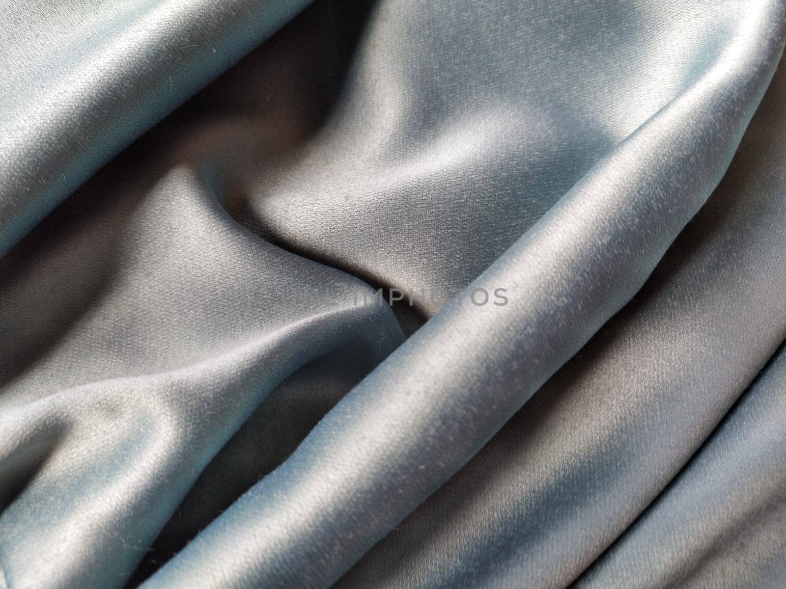 Silky to the touch fabric of gray - blue color with a brilliant shimmer. Natural lighting, light and shadow. The material is casually folded. Polyester Textile