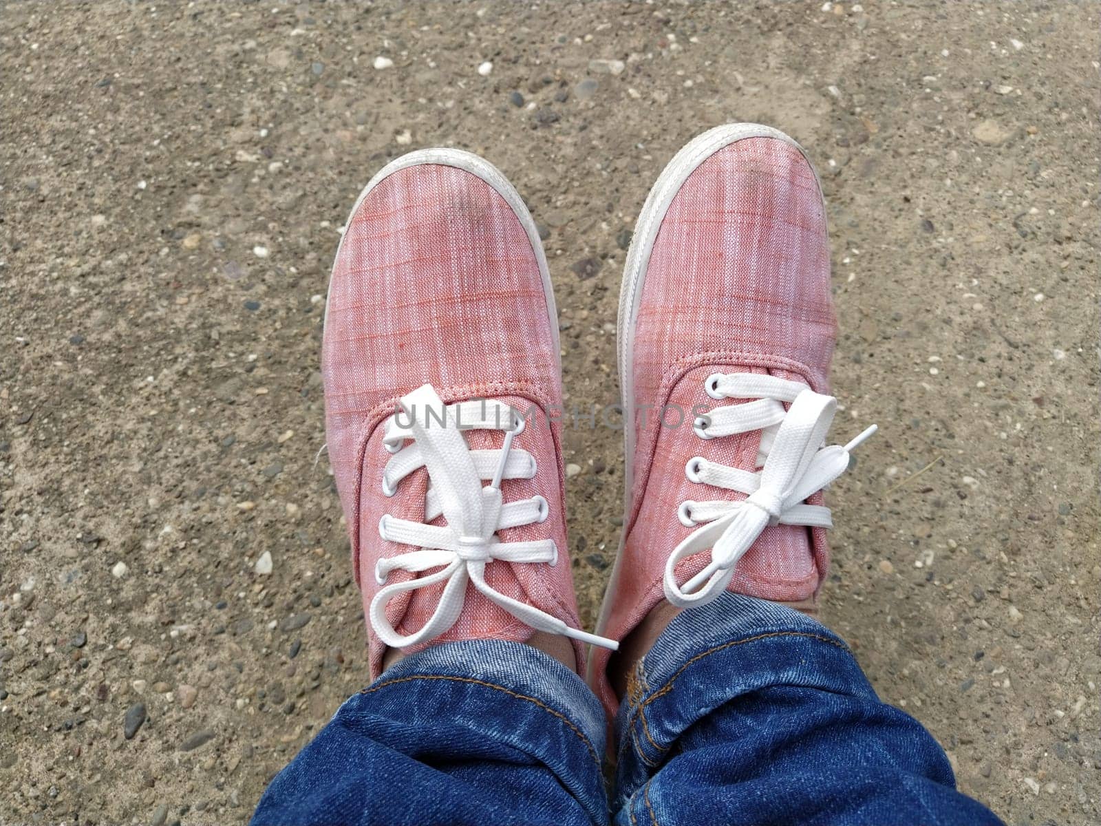 Pink sneakers with white laces on the legs. Blue jeans wrapped underneath. View from above. Carefree and sporty