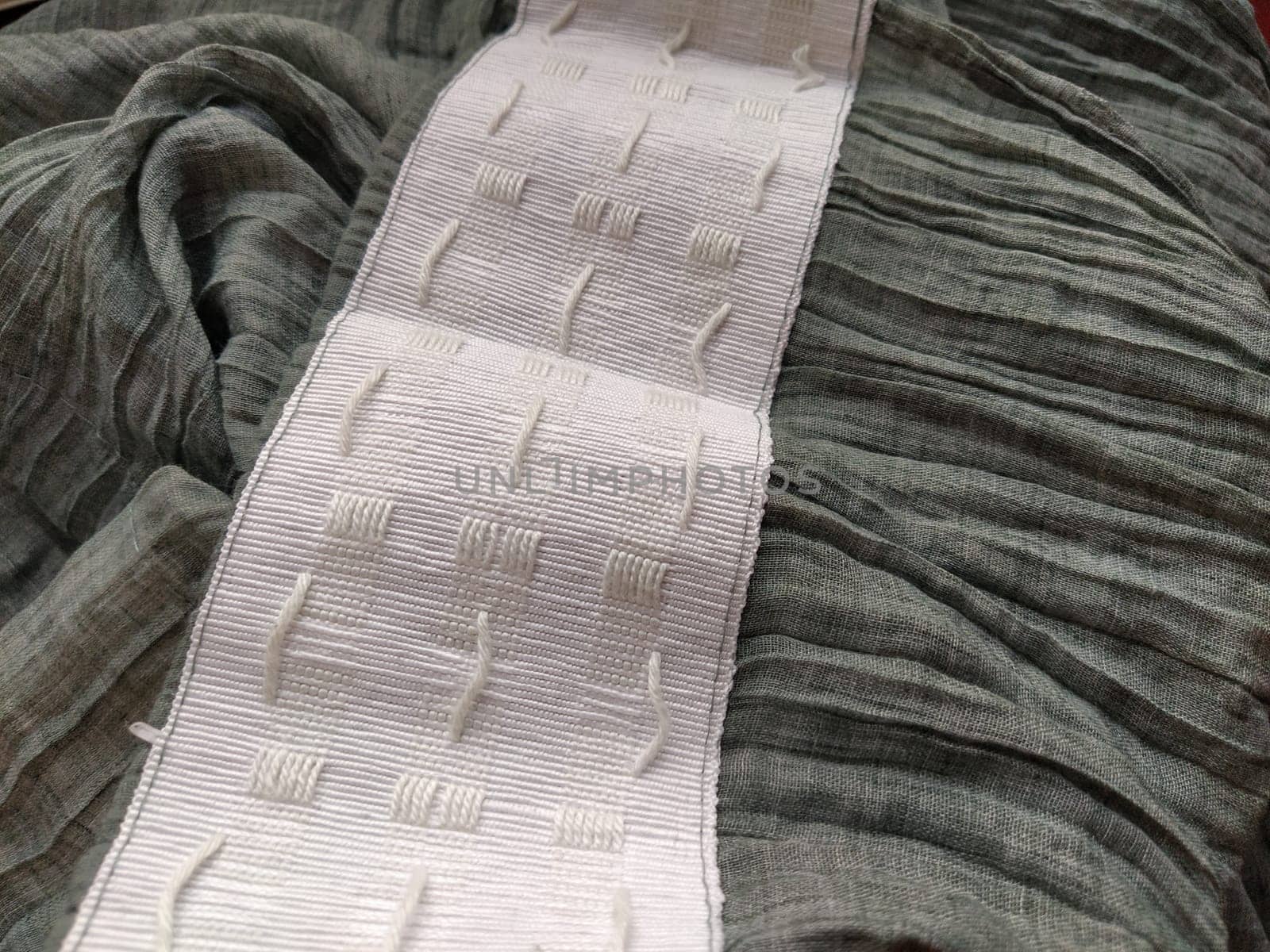 wide white curtain tape sewn to gray pleated fabric. Finishing the top of a curtain or light tulle