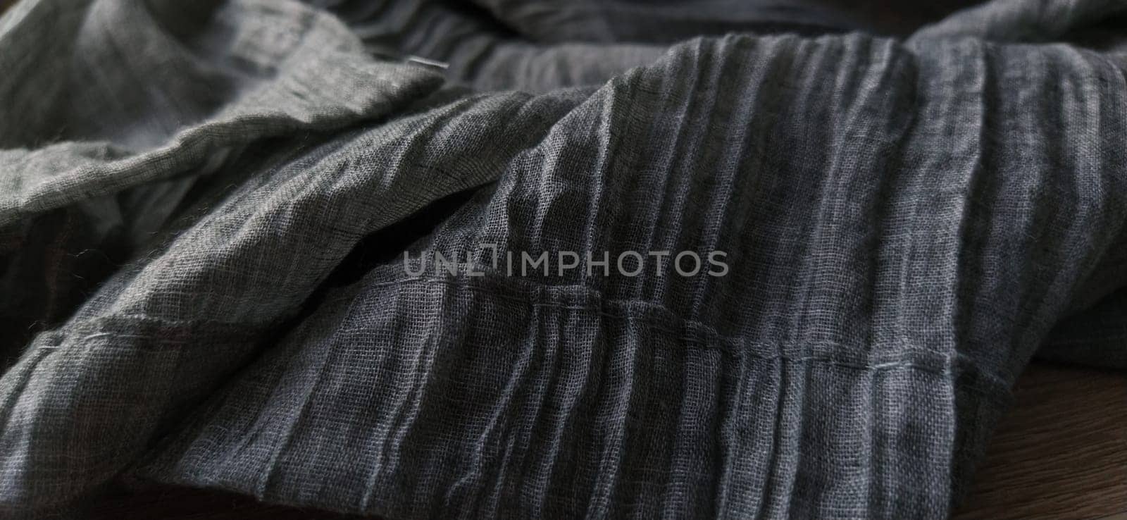 Gray pleated fabric or crumpled textile closeup. Light translucent curtains or tulle in the Scandinavian style. The lower edge of the curtain is hemmed 2-3 cm from the edge. Soft focus
