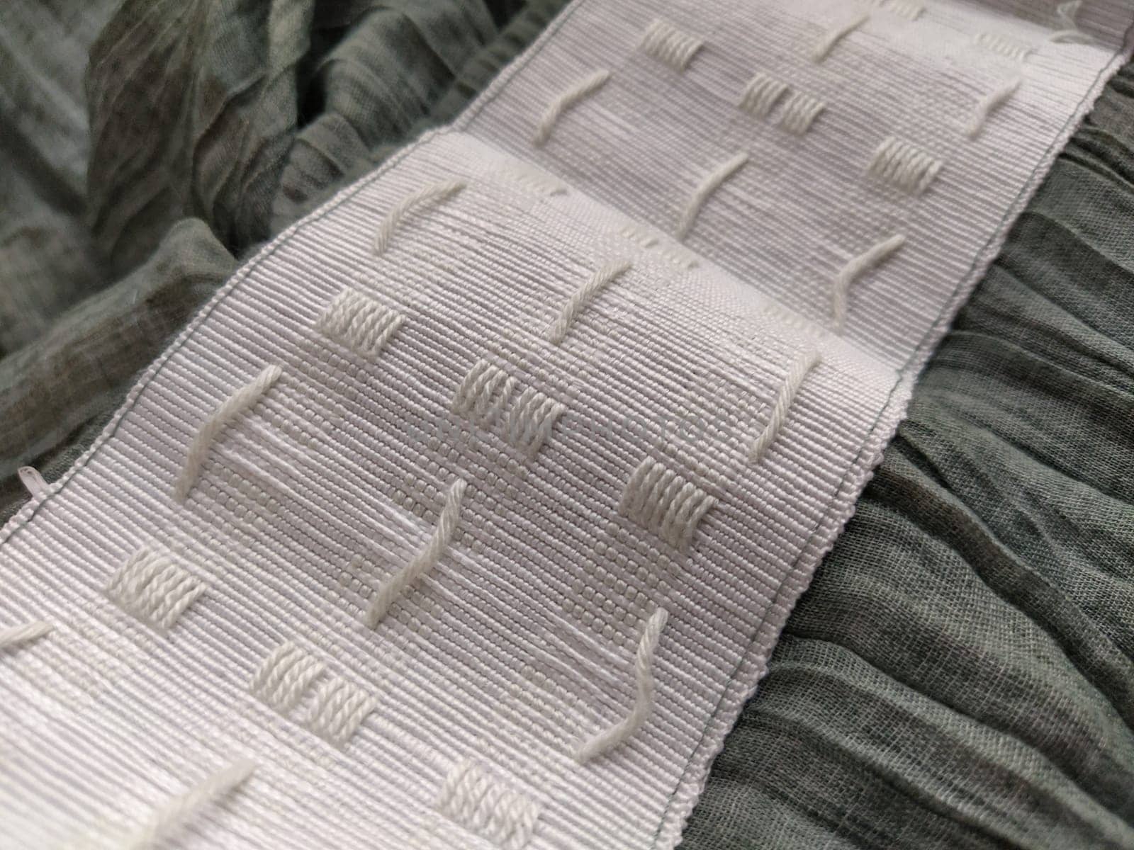 wide white curtain tape sewn to gray pleated fabric. Finishing the top of a curtain or light tulle.