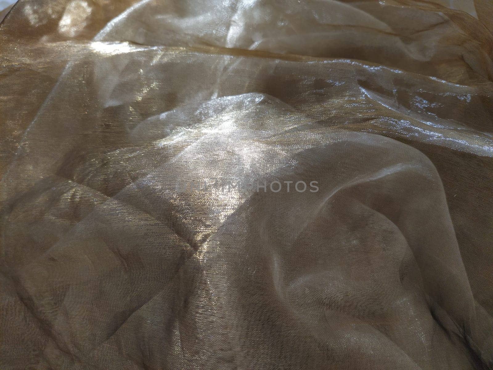 Organza is yellow-brown with a beige sheen. Shiny, reflective, beautiful fabric for curtains, tulles. Interior design option. Twisted, casually folded organza section in sunlight.