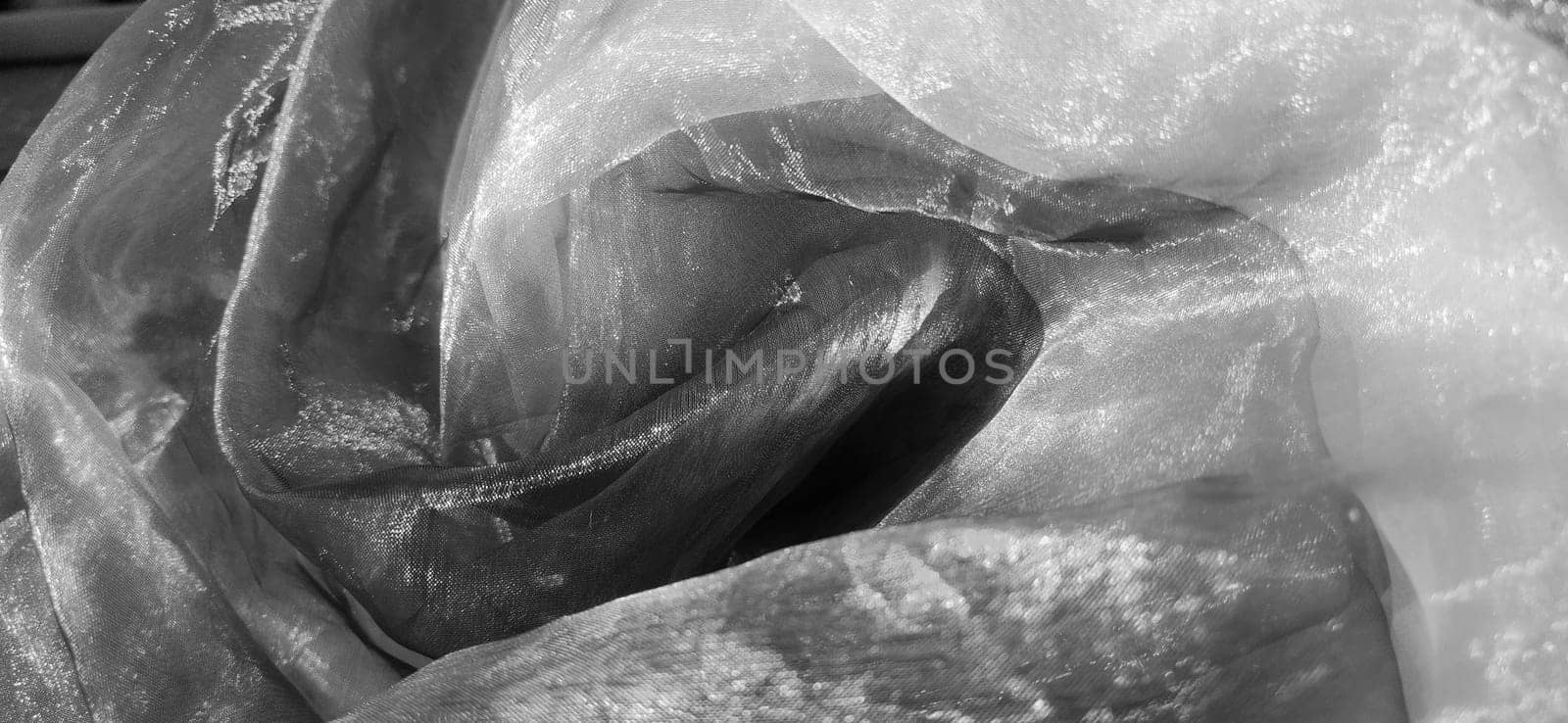Organza monochrome. Shiny, reflective, beautiful fabric for curtains, tulles. Interior design option. Twisted, casually folded organza section in sunlight.