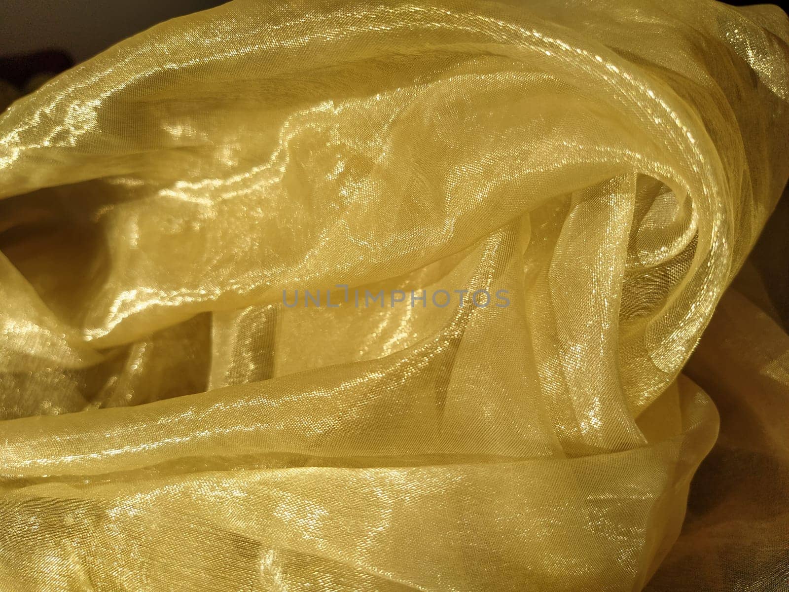 Organza is yellow-brown with a beige sheen. Shiny, reflective, beautiful fabric for curtains, tulles. Interior design option. Twisted, casually folded organza in sunlight.