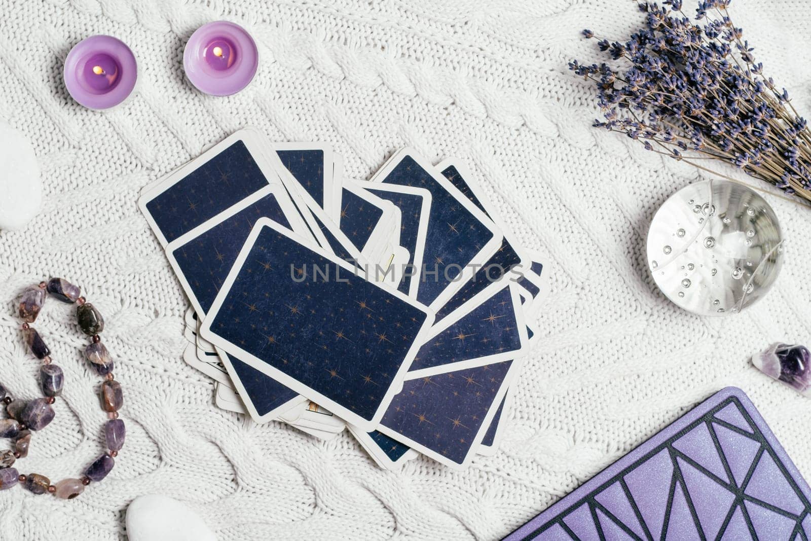 Tarot cards spread face down on white knitted surface with crystal ball, lavender, candles and accessories. Top view. Minsk, Belarus, 11.10.2021