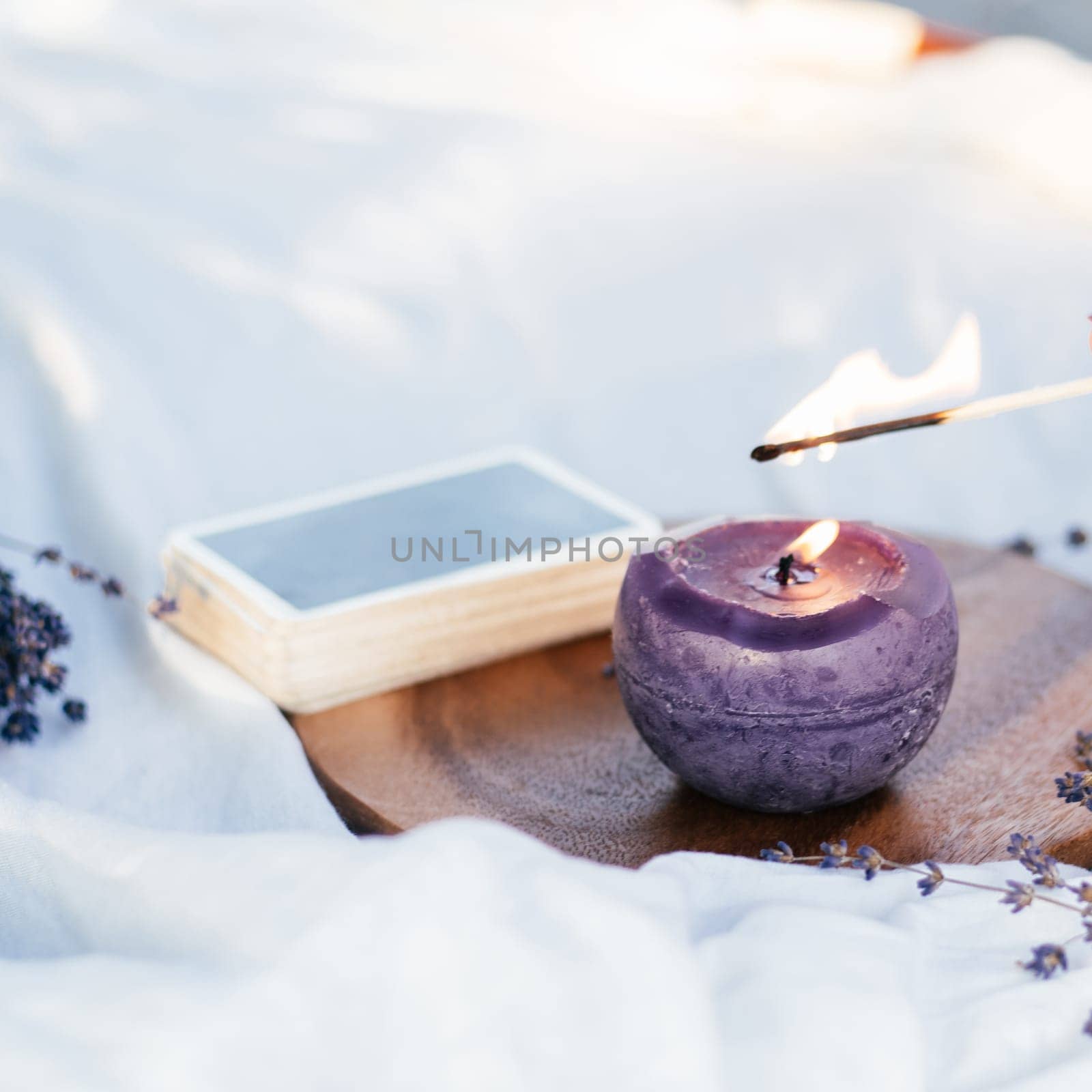 Match lights candle with next to deck of cards and lavender flowers on white and wooden surface