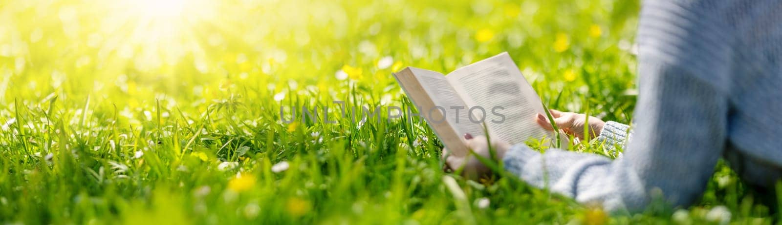 Woman lying on the blossoming meadow with book in her hands. Concept of the vacation and hobby.