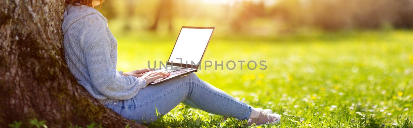 Woman with laptop sitting on the grass in the natural park. Concept of the freelance, working and learning.