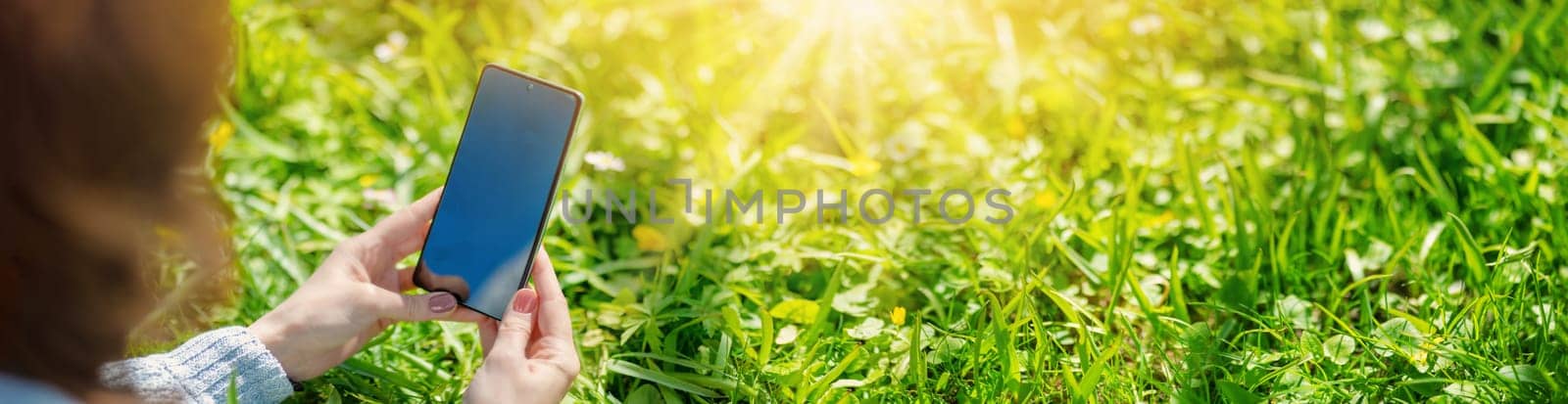 Woman holding in her hands smartphone with empty black screen. Panoramic view of the blossoming natural park.