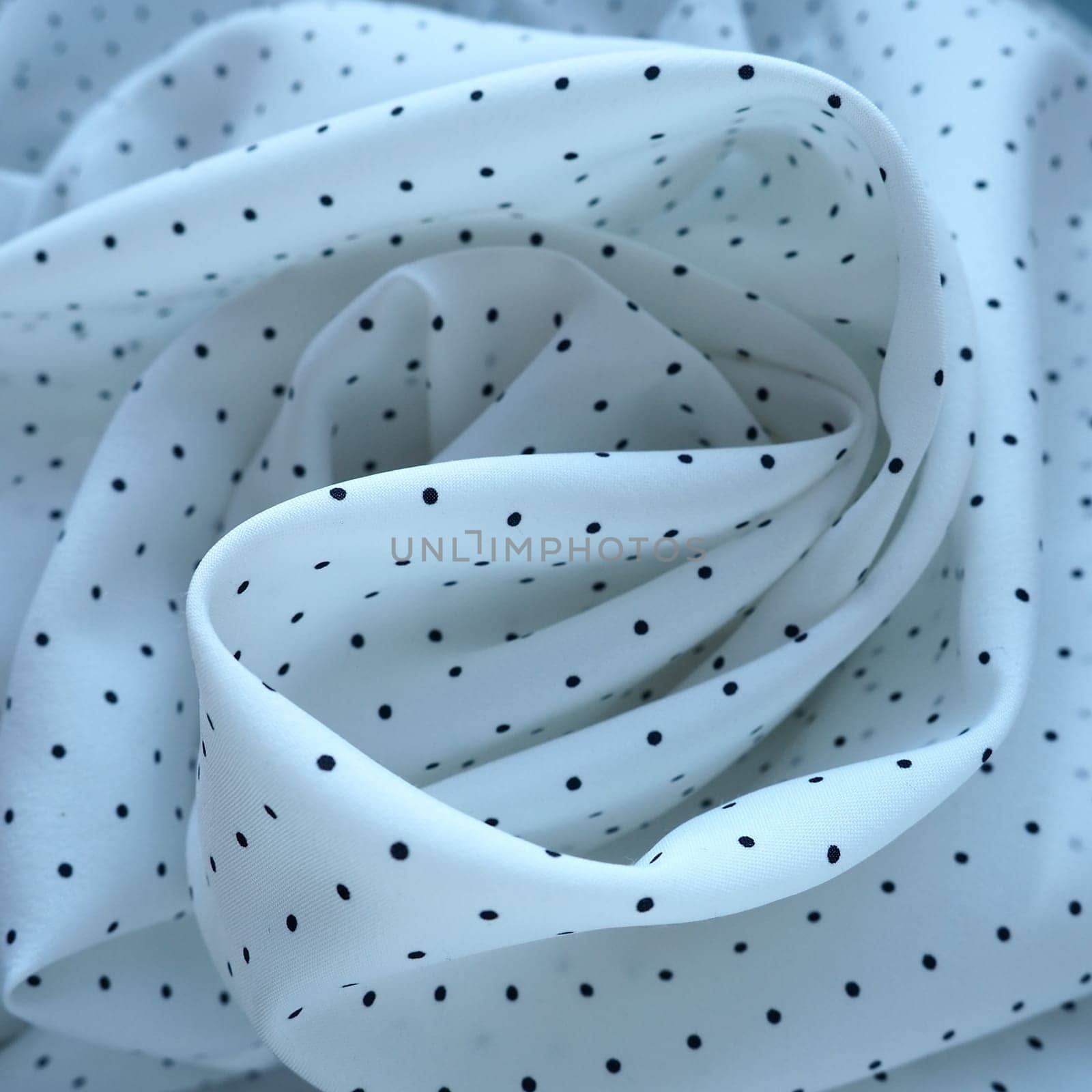 Texture of silk fabric. Black polka dots on a white background. Dress lightweight synthetic fabric in white with a repeating pattern. The textile is made up of waves and folds. Feminine classic style