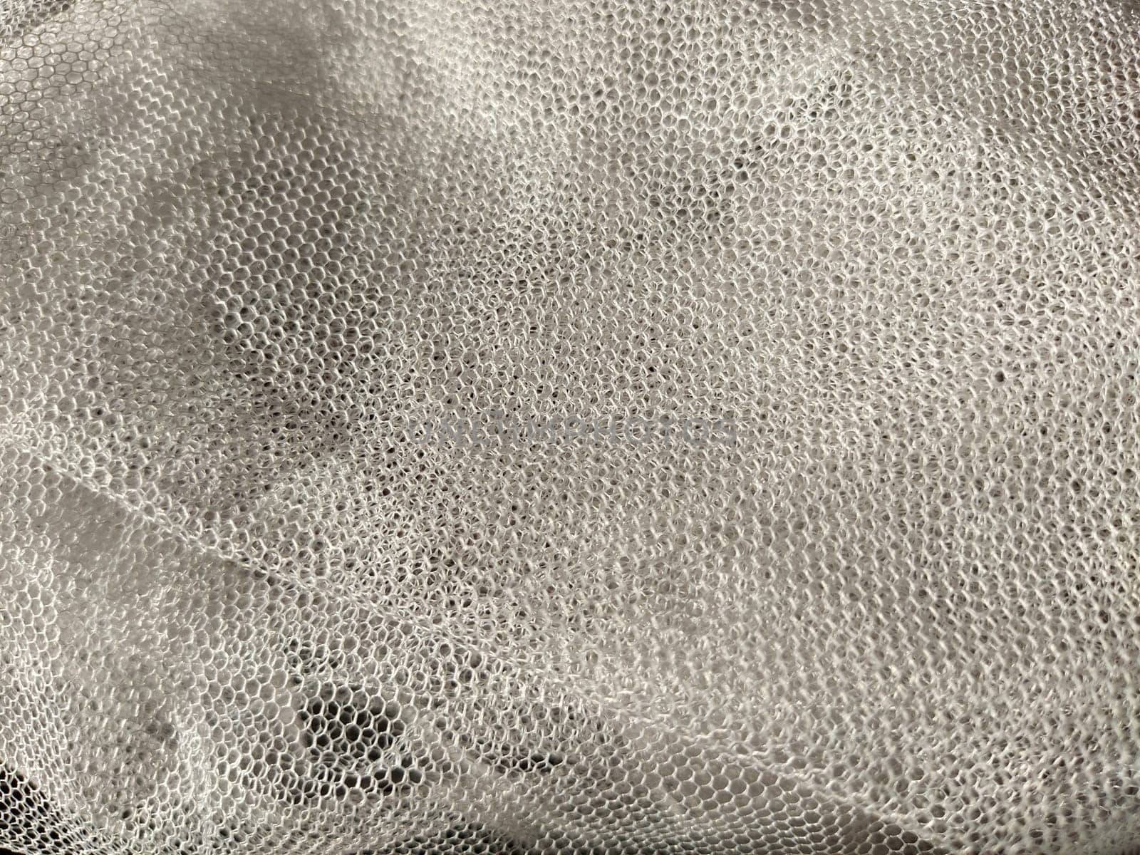 Sheer white net-like tulle. Mesh fabric wrinkled or folded carelessly. Close-up.