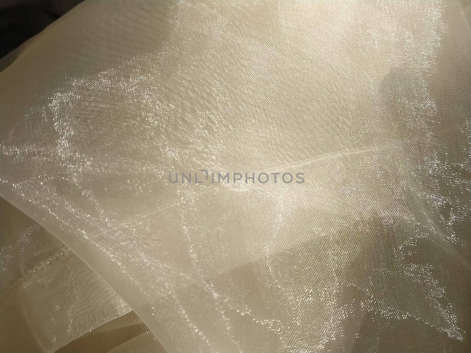 Organza in white and beige or champagne color close-up. Lightweight sheer tulle curtains under side lighting.