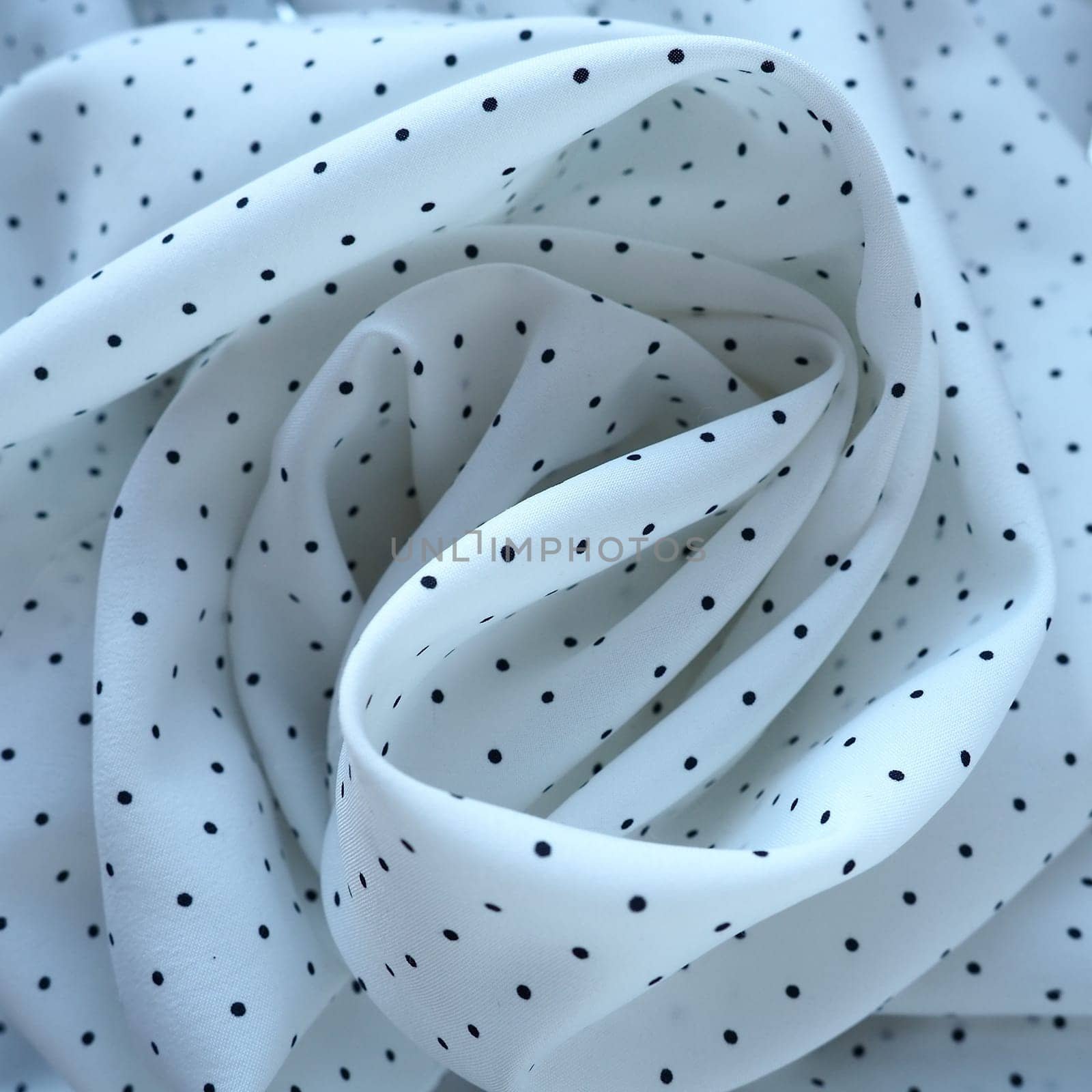 Texture of silk fabric. Black polka dots on a white background. Dress lightweight synthetic fabric in white with a repeating pattern. The textile is made up of waves and folds. Feminine classic style