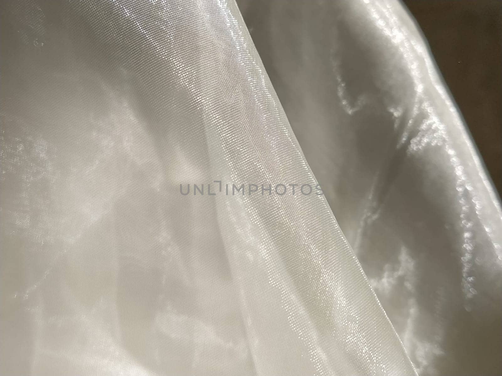 Organza in white and beige or champagne color close-up. Lightweight sheer tulle curtains under side lighting.