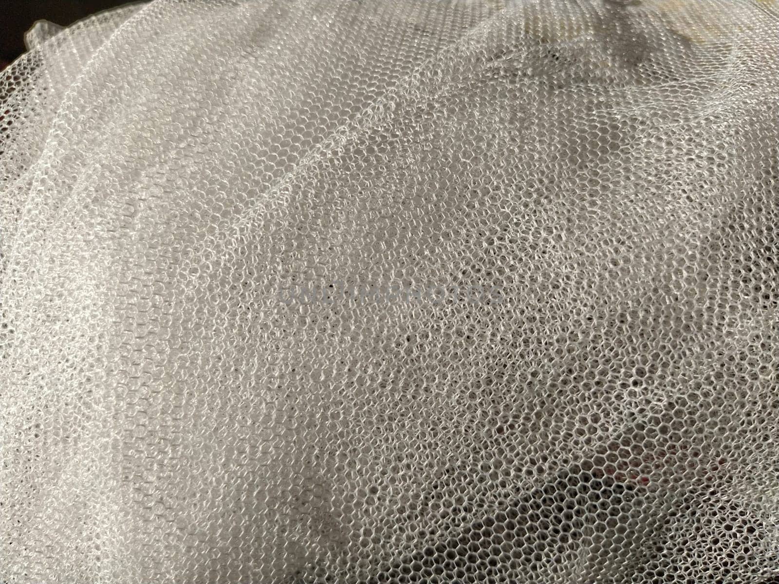Sheer white net-like tulle. Mesh fabric wrinkled or folded carelessly. Close-up.