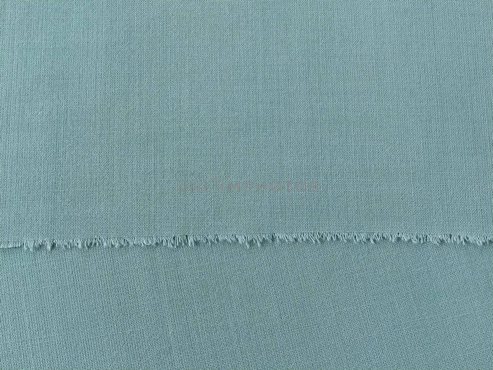 Ripped edge of fine woolen fabric in green or blue. Loose threads at the edge of a piece of textile. Close-up. Woven background. Calm green pastel color.