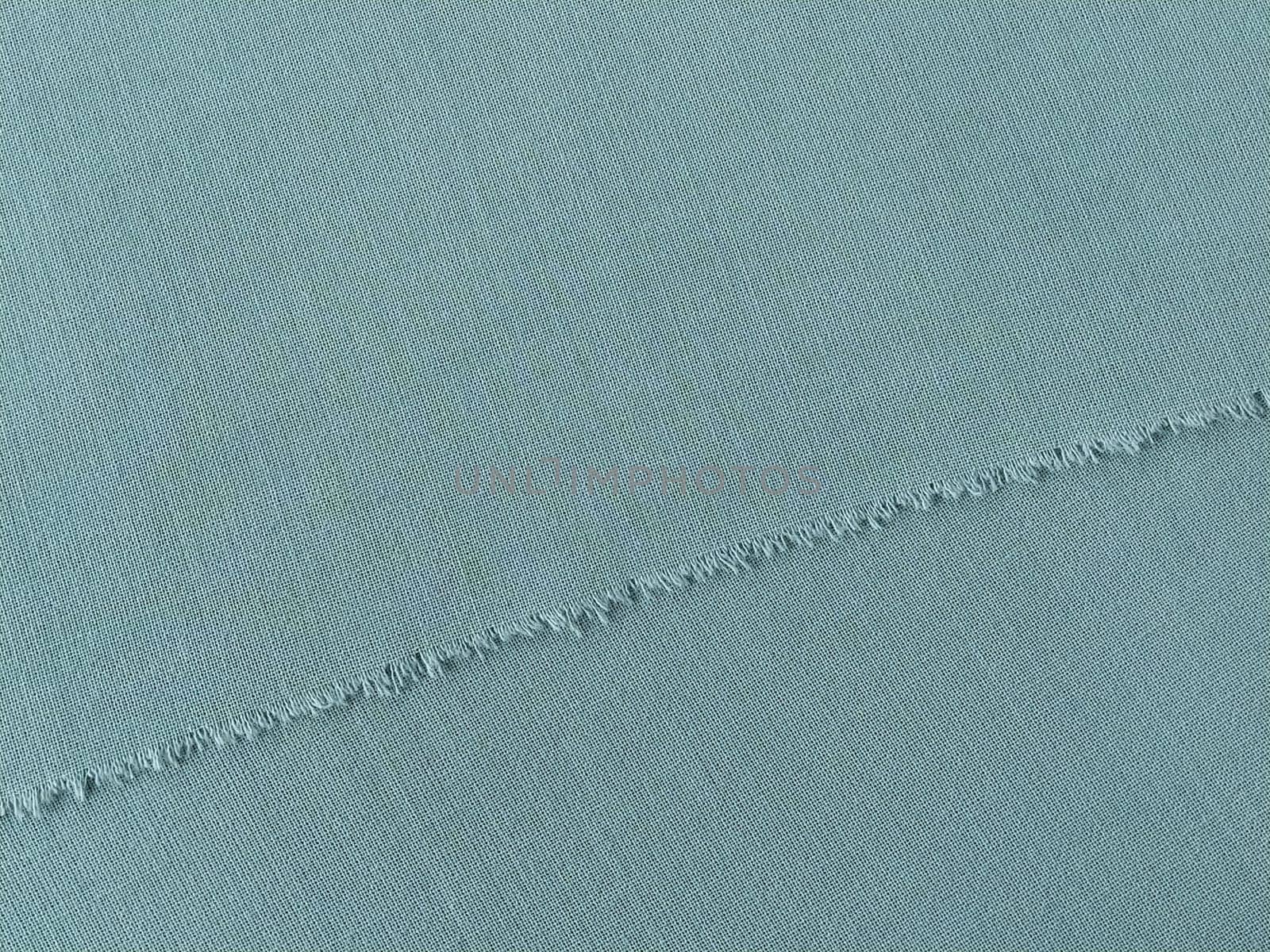 Ripped edge of fine woolen fabric in green or blue. Loose threads at the edge of a piece of textile. Close-up. Woven background. Calm green pastel color.