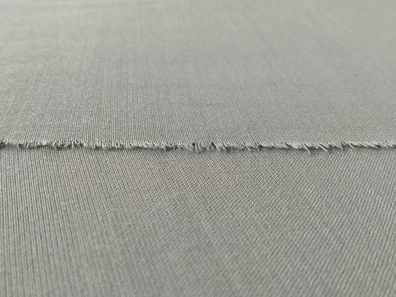 Ripped edge of fine woolen fabric in green or blue. Loose threads at the edge of a piece of textile. Close-up. Woven background. Calm green pastel color.