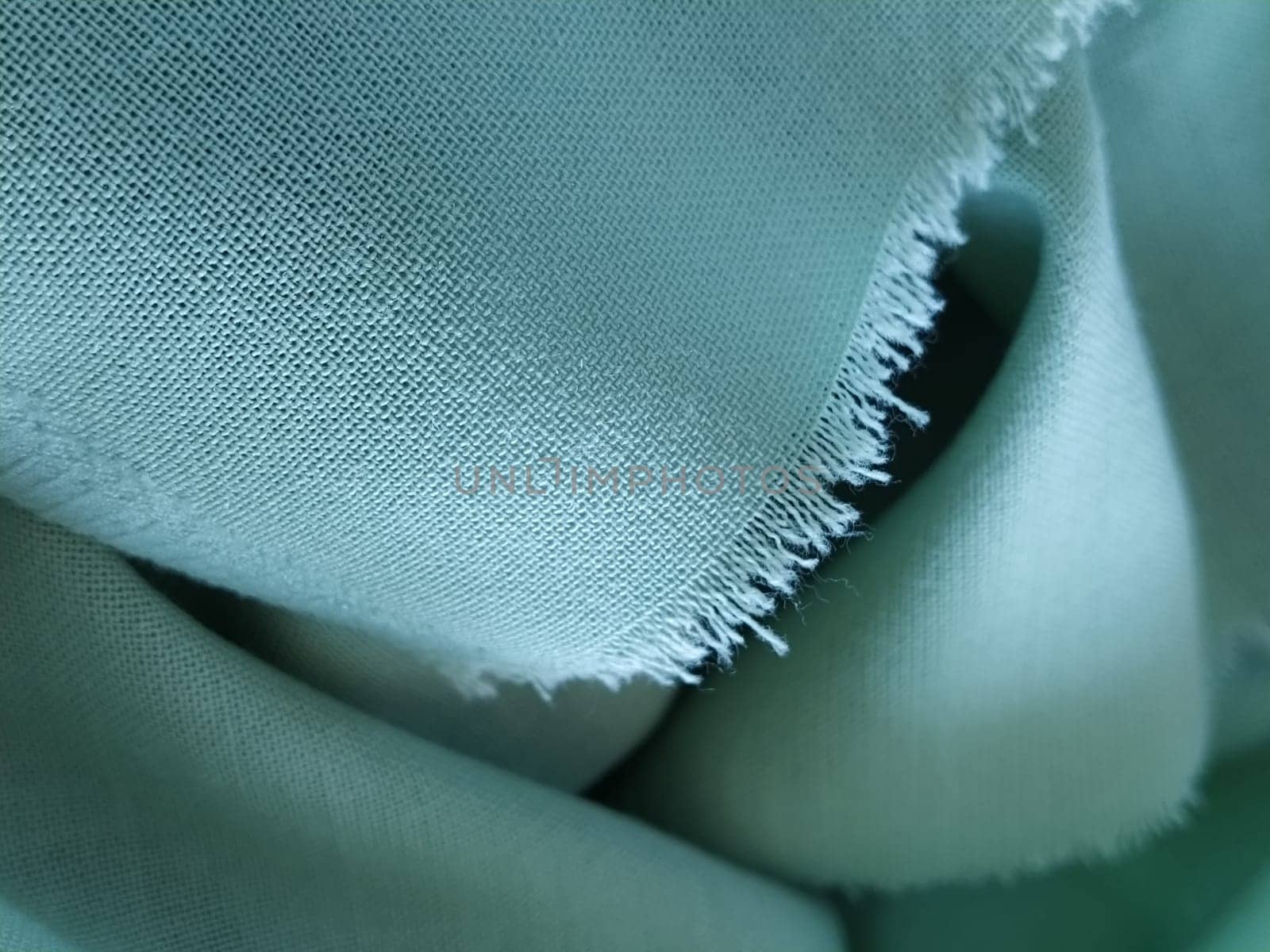 Close up of a woolen fabric of green color. Abstract canvas background, empty template. Thin natural fabric, wool or linen. The edge of the fabric is treated against chapping.