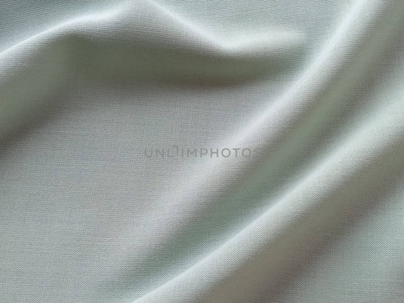 Beautifully folded light green fabric. Soft pleasant waves and flounces on textiles. Close-up. Drapery for curtains, fabric for dressmaking or upholstery.
