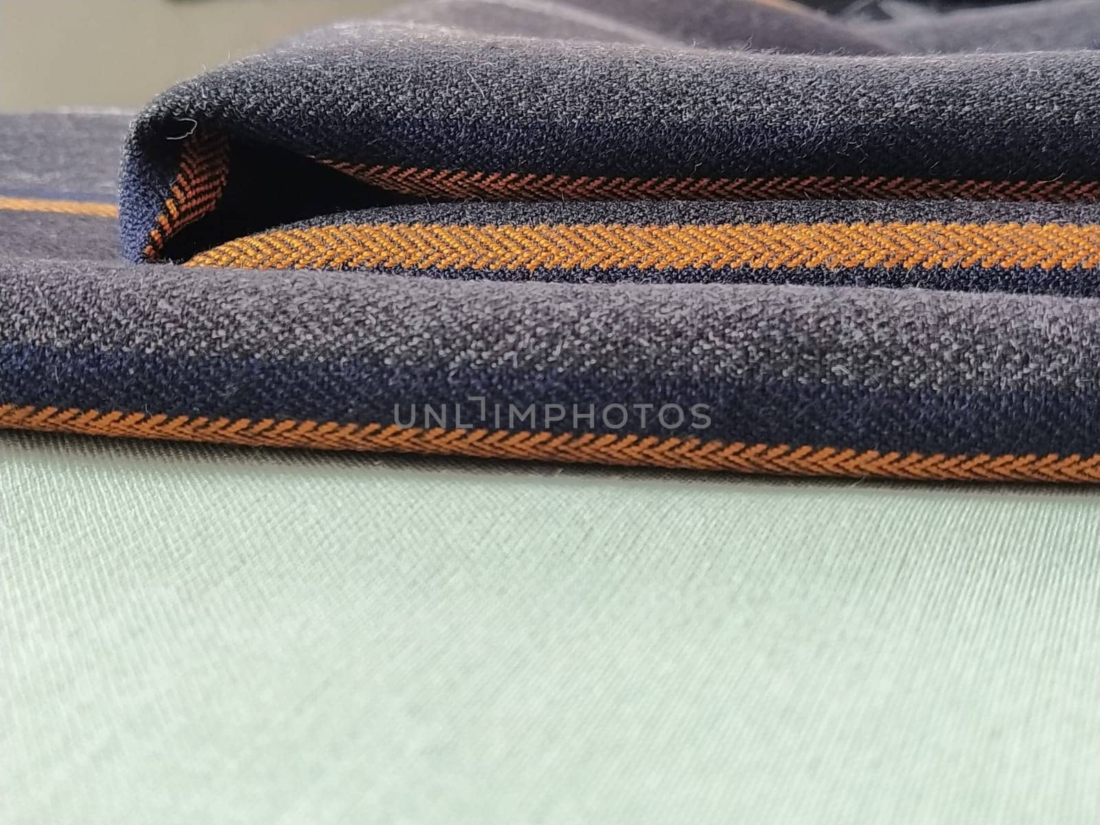 Gray-black fabric with orange and blue stripes. Textile fabric folded neatly on the surface. Natural wool material for sewing clothes and upholstery. Lifestyle. Close-up. Soft focus.
