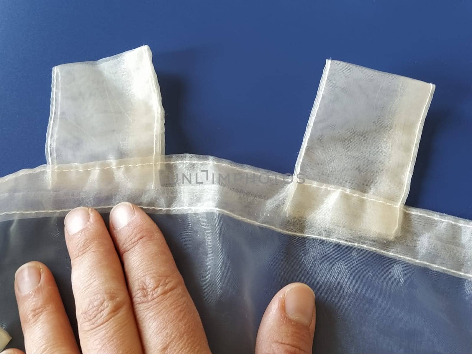 A seamstress's hand on a transparent organza. Loops on the tulle curtain. Sewing curtains. Blue background.