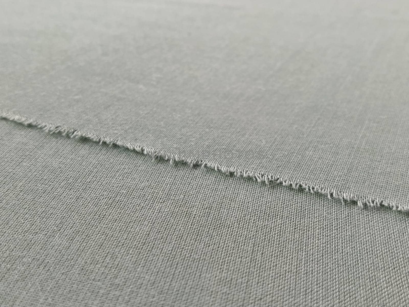 Ripped edge of fine fabric in gray. Loose threads at the edge of a piece of textile. Close-up. Woven background. Calm pastel color.