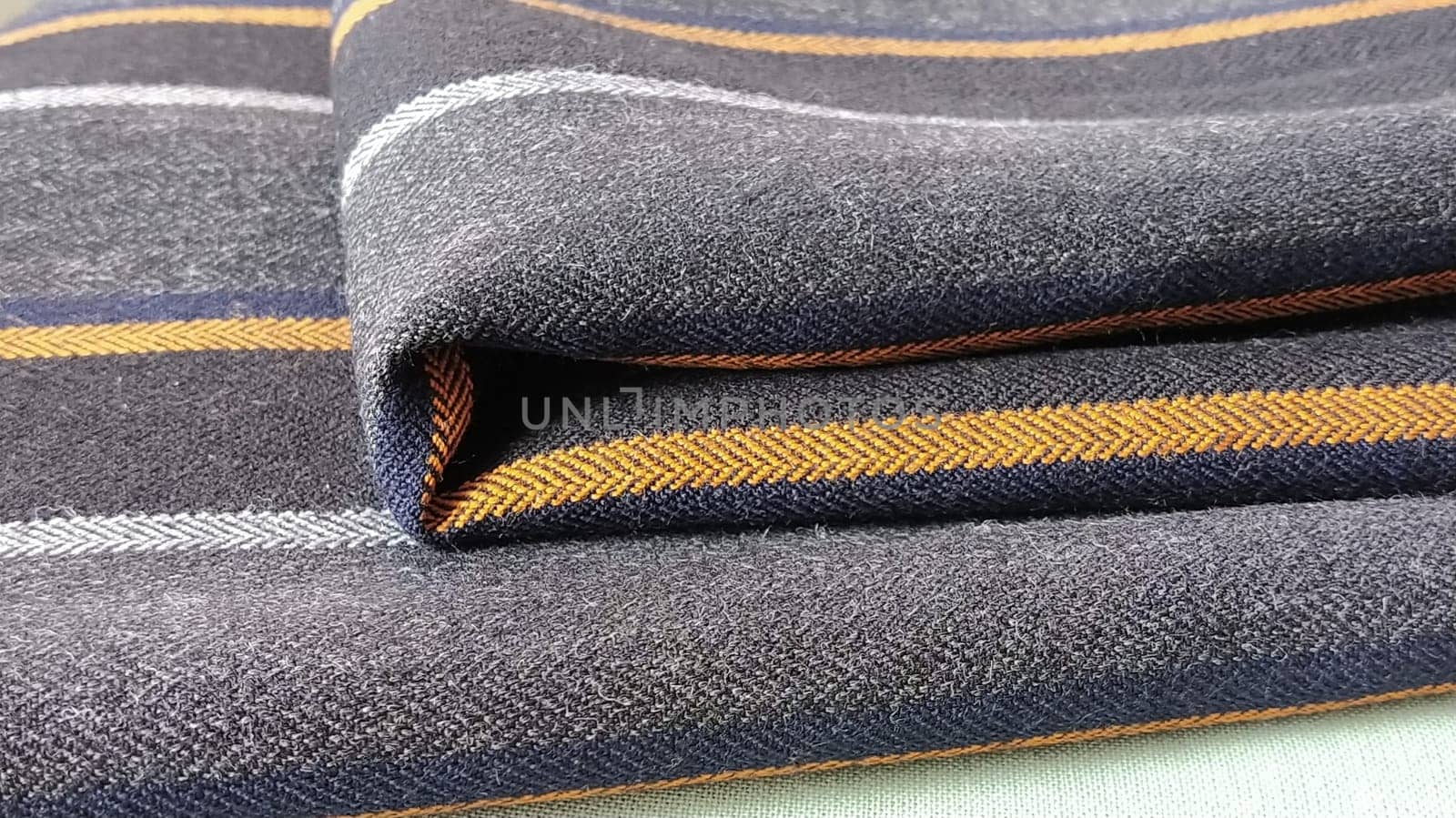 Light green and black-gray folded fabric with orange and dark blue stripes. Interior decoration. Dress fabrics in casual style. Dense material for indoor curtains and furniture finishing.