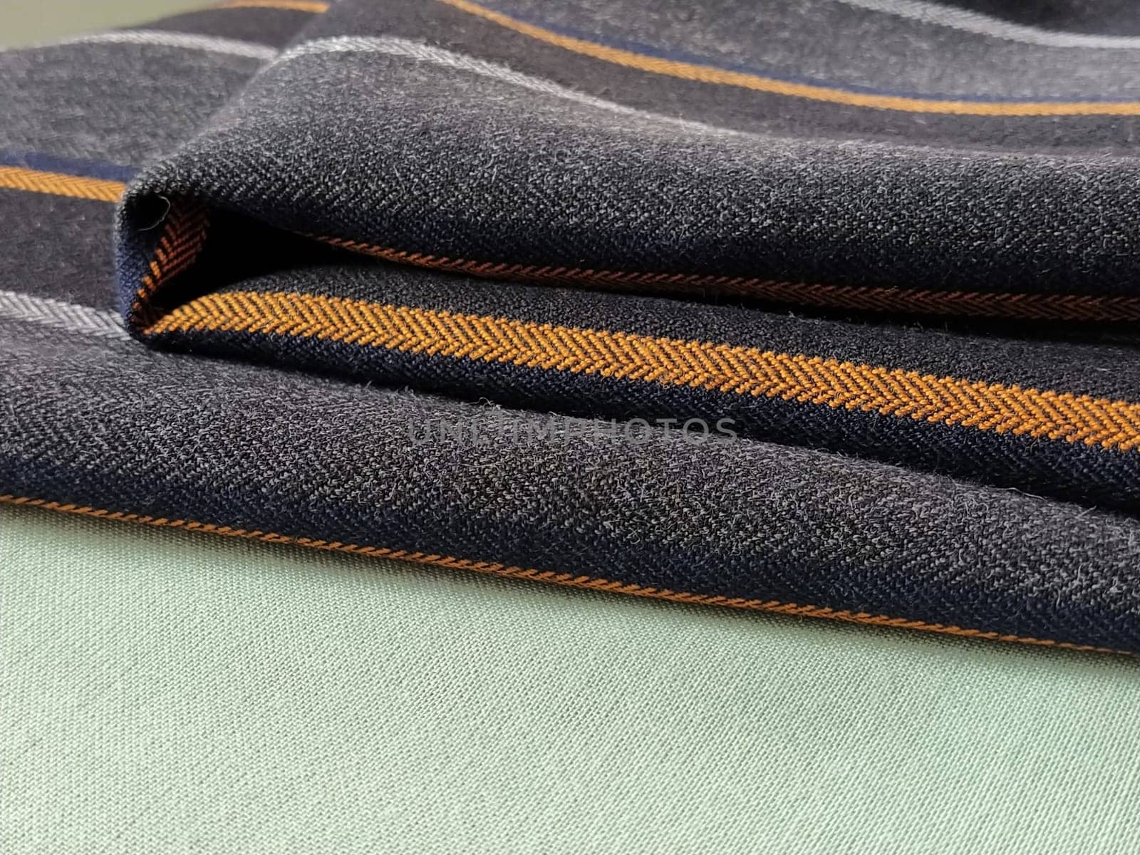 Light green and black-gray folded fabric with orange and dark blue stripes. Interior decoration. Dress fabrics in casual style. Dense material for indoor curtains and furniture finishing.