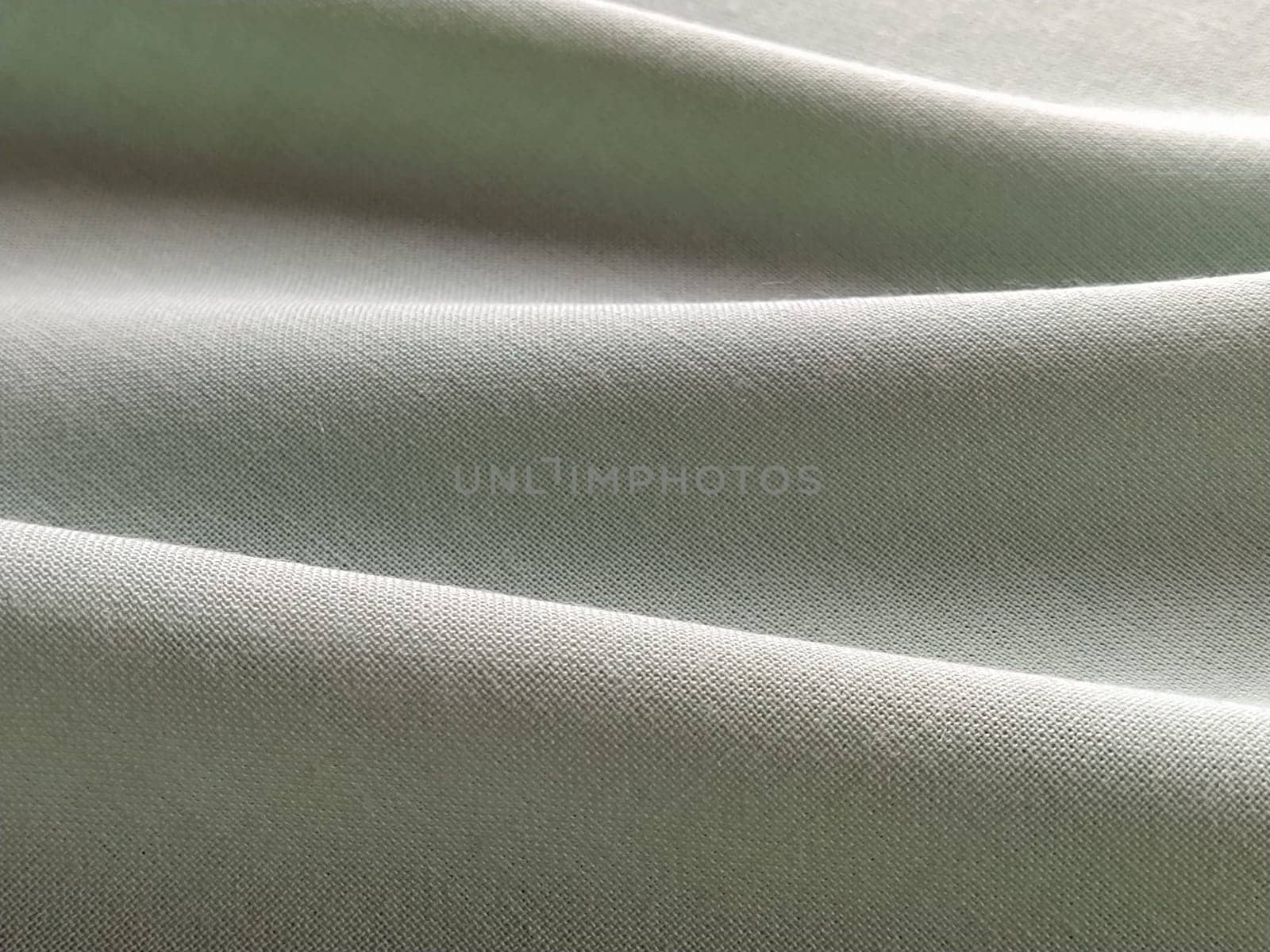 Beautifully folded light green fabric. Soft pleasant waves and flounces on textiles. Close-up. Drapery for curtains, fabric for dressmaking or upholstery.