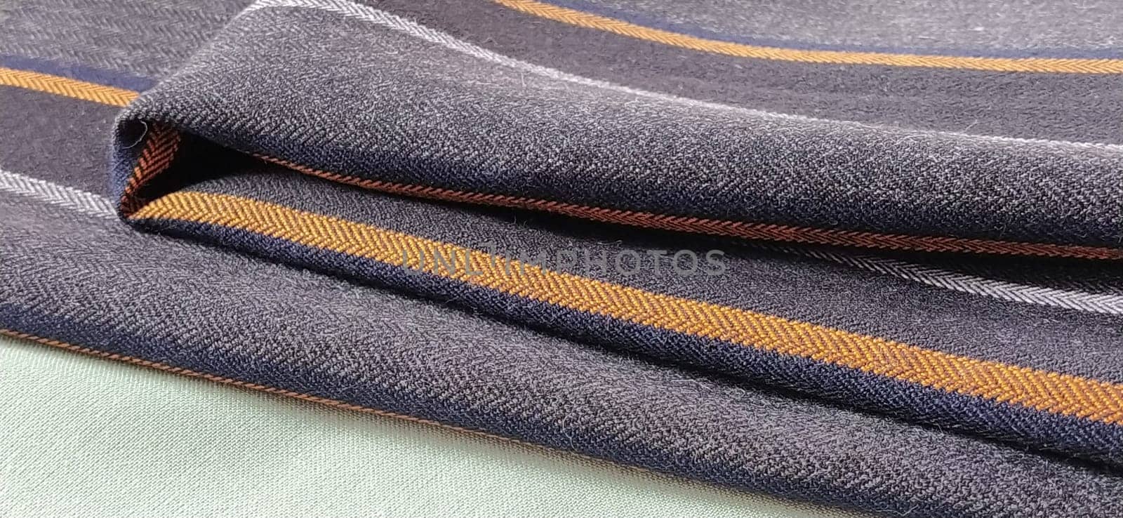 Light green and black-gray folded fabric with orange and dark blue stripes. Interior decoration. Dress fabrics in casual style. Dense material for indoor curtains and furniture finishing.