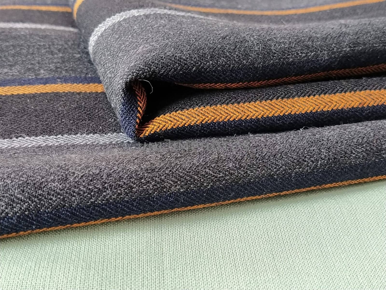 Light green and black-gray folded fabric with orange and dark blue stripes. Interior decoration. Dress fabrics in casual style. Dense material for indoor curtains and furniture finishing.
