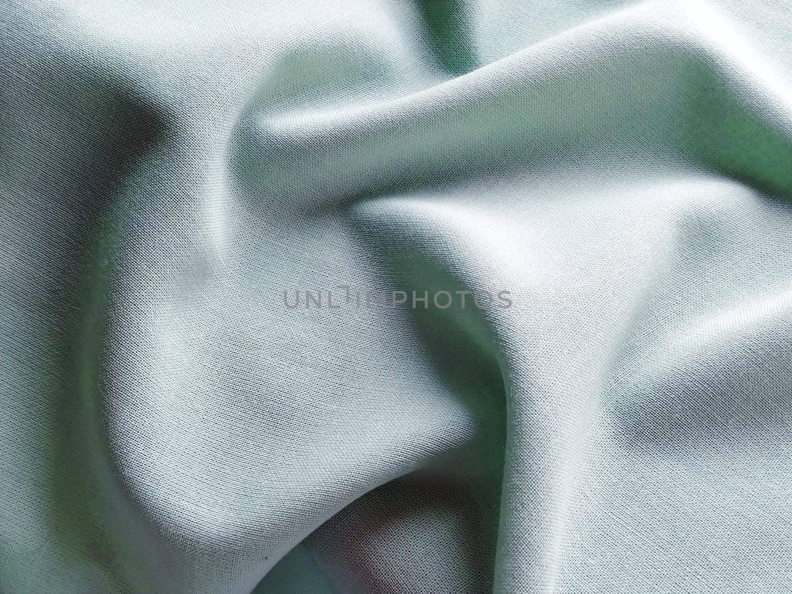 Beautifully folded light green fabric. Soft pleasant waves and flounces on textiles. Close-up. Drapery for curtains, fabric for dressmaking or upholstery.