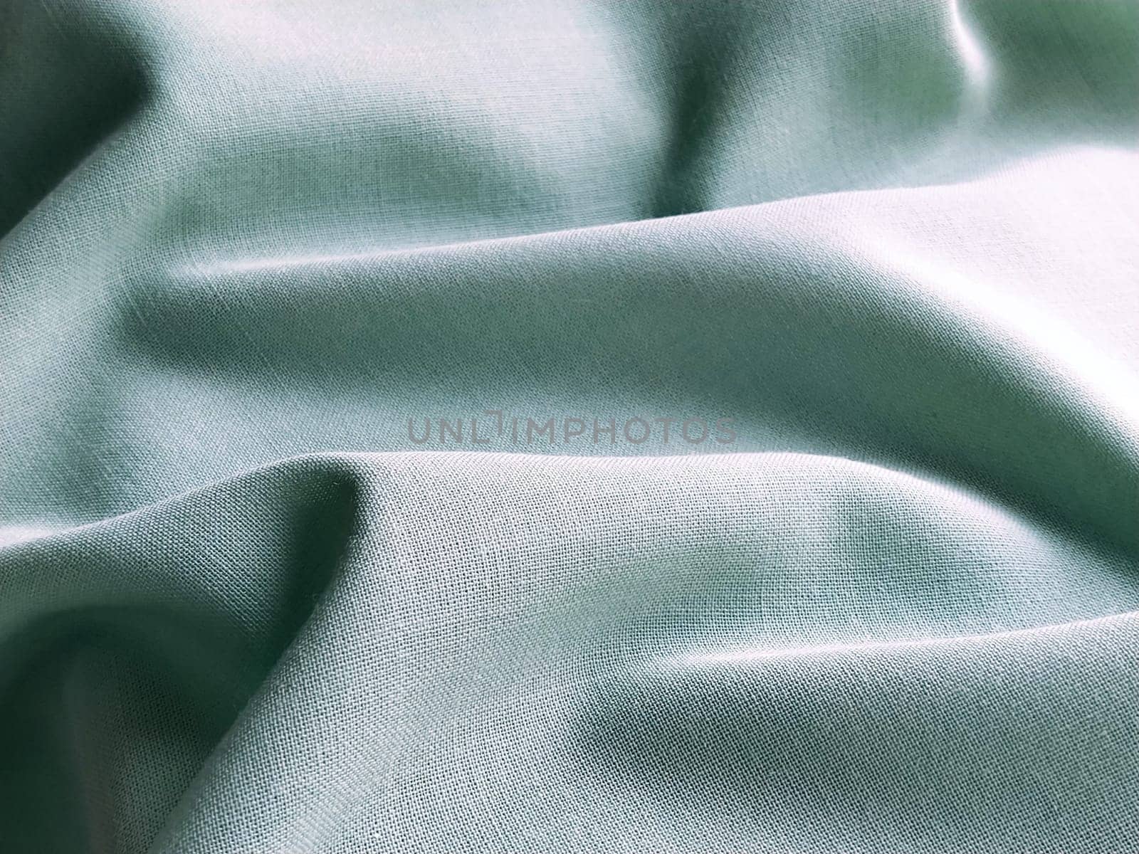 Beautifully folded light green fabric. Soft pleasant waves and flounces on textiles. Close-up. Drapery for curtains, fabric for dressmaking or upholstery.