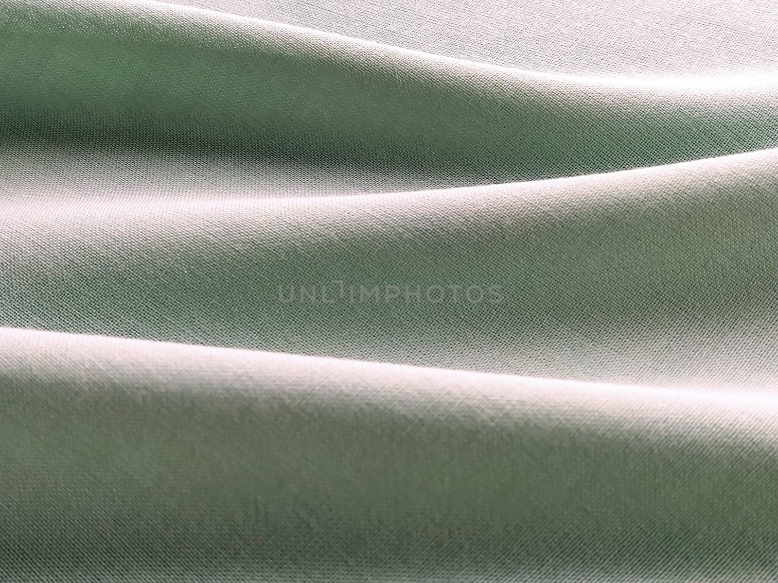 Beautifully folded light green fabric. Soft pleasant waves and flounces on textiles. Close-up. Drapery for curtains, fabric for dressmaking or upholstery.