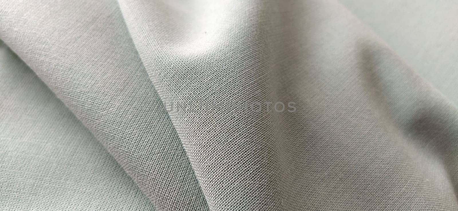 white fabric with interlacing threads close-up. Light green tint. Nice beautiful waves on the material. A neatly folded piece of fabric. Interior decoration, tailoring. Textile industry.
