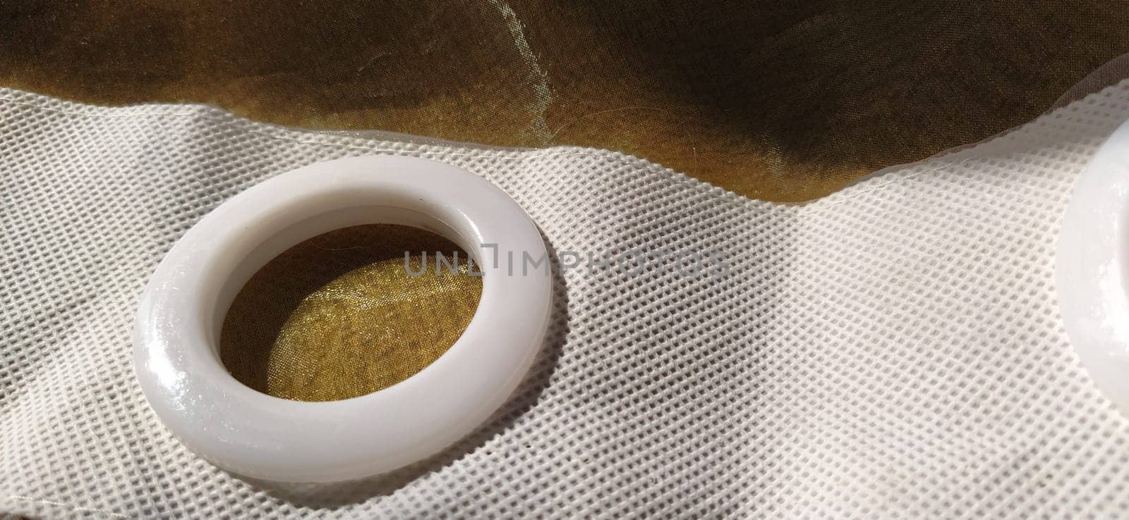Plastic rings for attaching the fabric to the curtain rod. White plastic organza tulle eyelets. Light curtain in beige, brown or orange colors. White non-woven fabric. Finished textile edge. Interior element