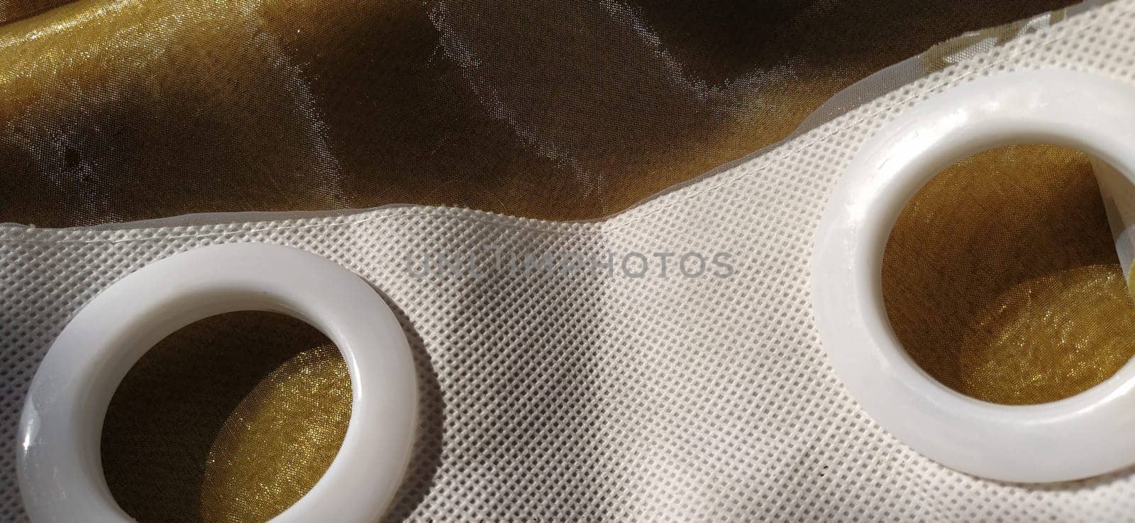 Plastic rings for attaching the fabric to the curtain rod. White plastic organza tulle eyelets. Light curtain in beige, brown or orange colors. White non-woven fabric. Finished textile edge. Interior element