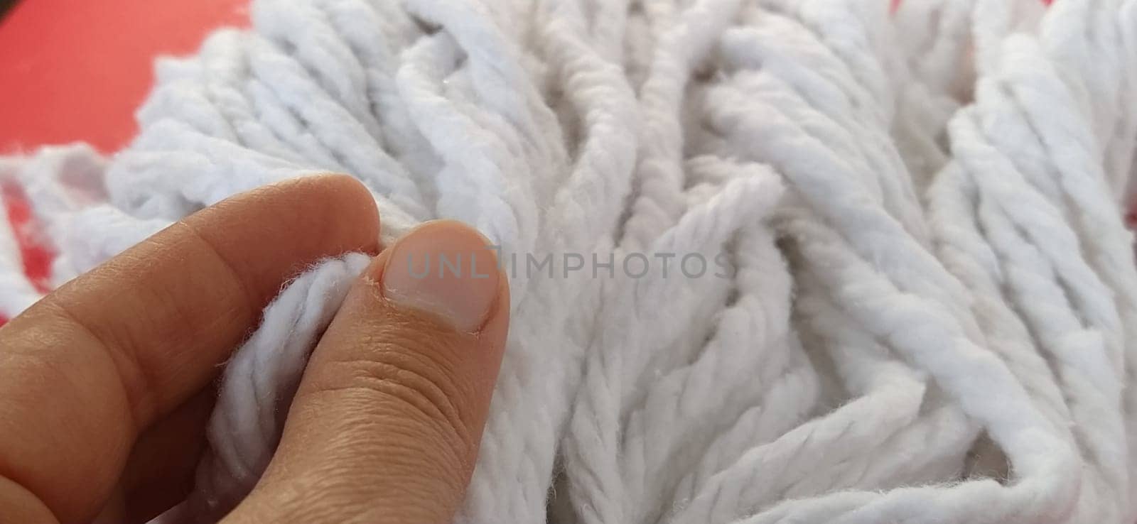 A woman's hand touches the cotton threads of the mop head. Choosing a mop for cleaning. Household cleaning work. White ropes. Cleaning lady's fingers
