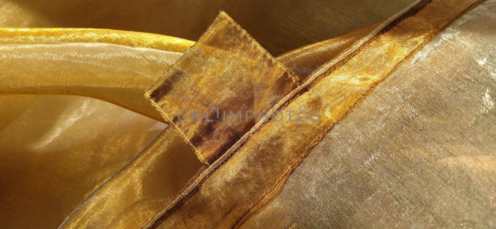 Curtain loops. Beautiful gold fabric. Organza in yellow, orange, beige and brown shades. Pleats in the fabric. Shiny gradient under the light. Folded silky tulle. Transparent curtain material. Banner