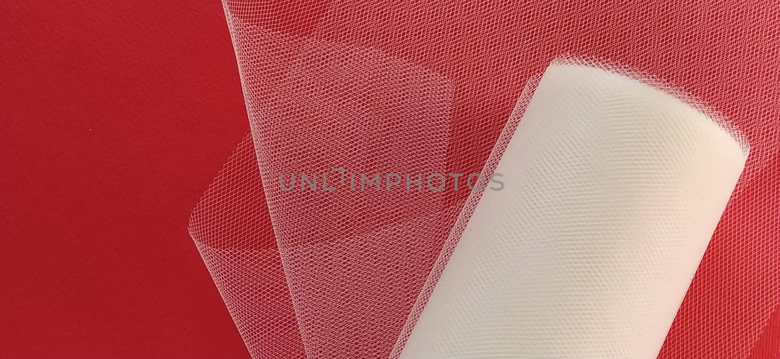 Fabric - white mesh in a roll on a red background. Nylon tape for tying bows on hair. A skein of tulle fabric. Copy space.