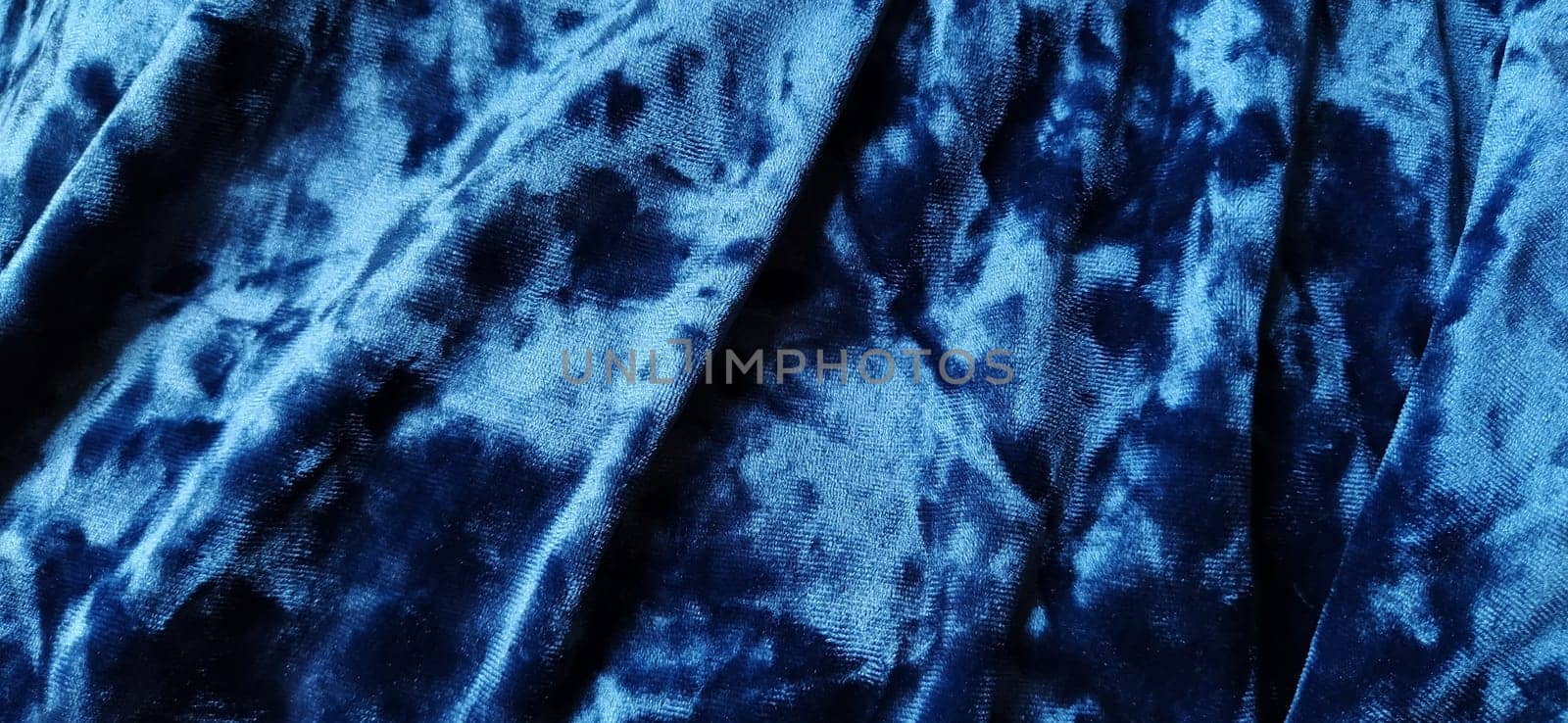 Velvet velor cloth background with glowing light and dark shadows. Background for theater and fashion design themes. Nice blue fabric with overflow. Soft focus.