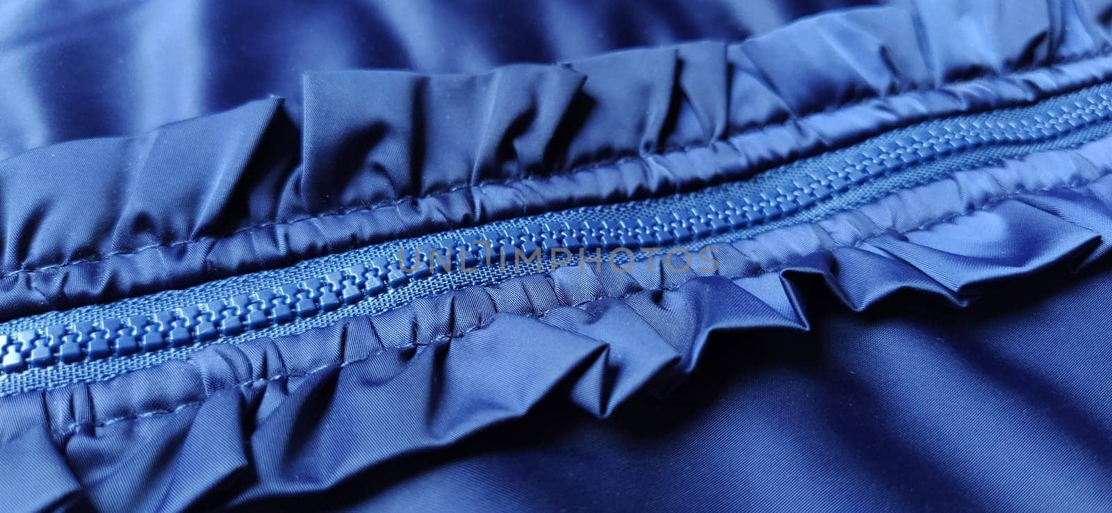 Buttoned zip on a blue raincoat. Waves and folds in the fabric. Beautiful flounces, ruffles, frills. Decorative finishing of a garment. Smocked, sewn silk fabric. Nice casual wear