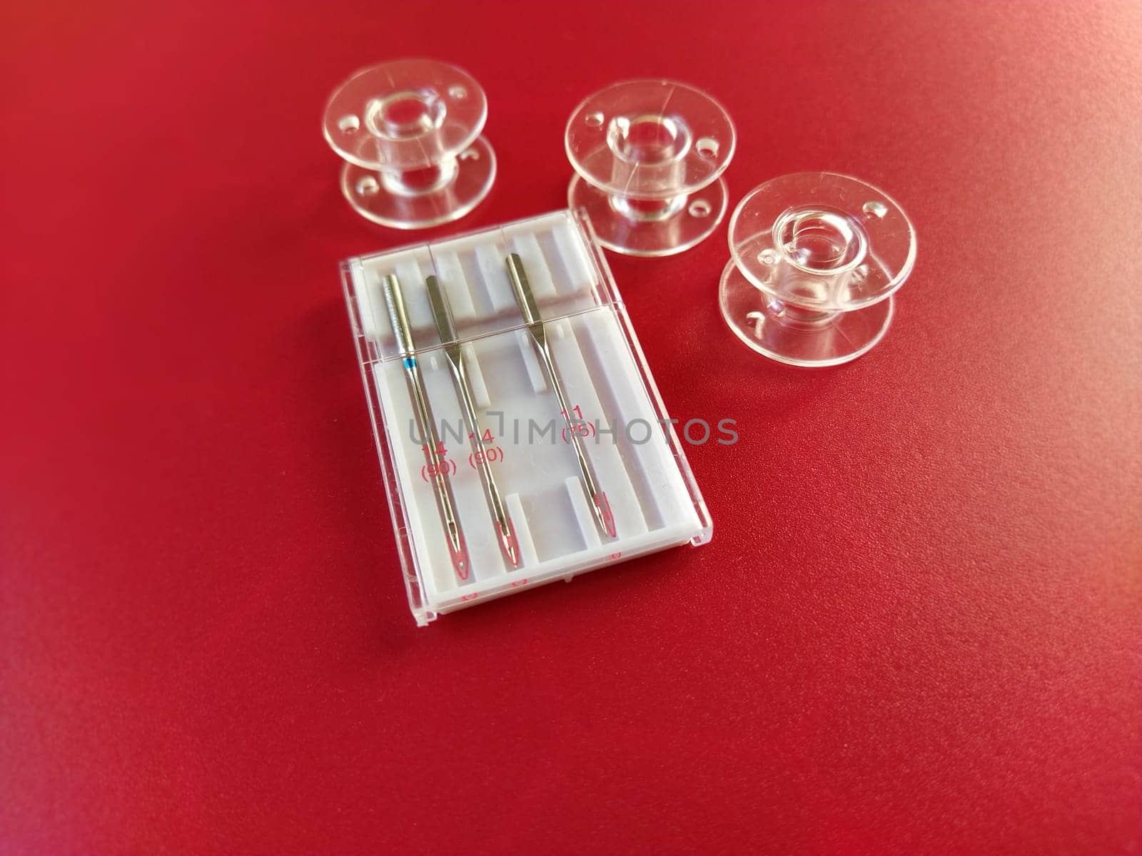plastic bobbins and a set of sewing machine needles on a red background.