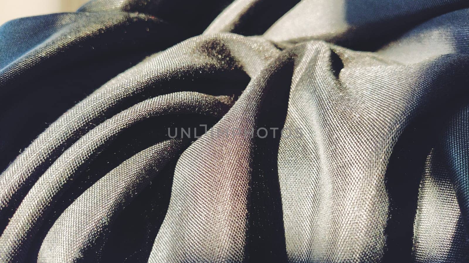 black fabric with interlacing threads close-up. Dark blue tint. Nice beautiful waves on the material. A neatly folded fabric. Interior decoration, sewing clothes and curtains. Textile industry.