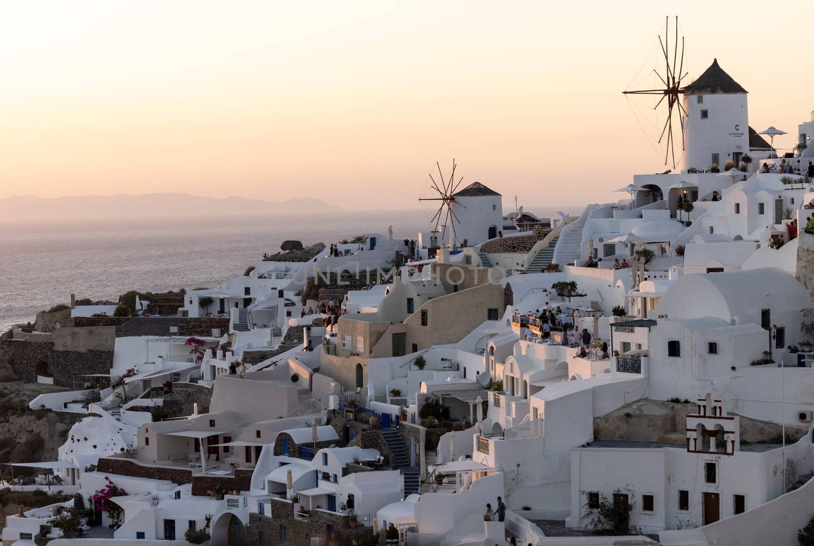 Oia, Santorini, Greece - June 28, 2021: Whitewashed houses and windmills in Oia in warm rays of sunset on Santorini island. Greece