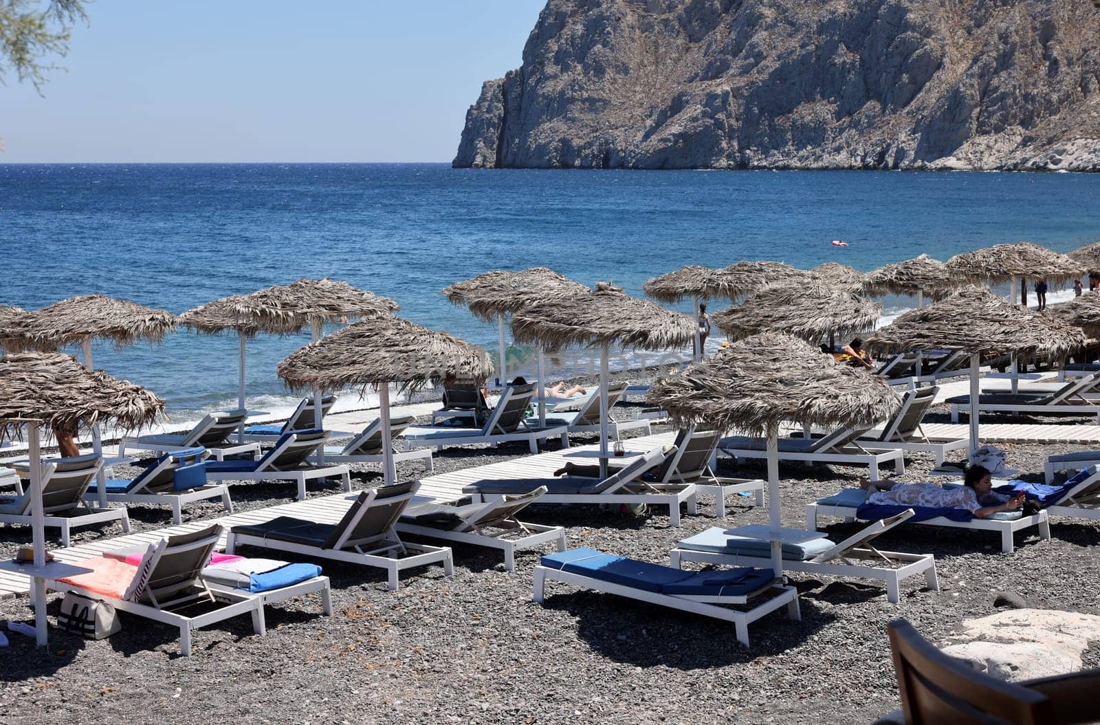 Kamari, Santorini, Greece - June 30, 2021: Sun loungers on the black volcanic beach of Kamari in Santorini. Cyclades, Greece