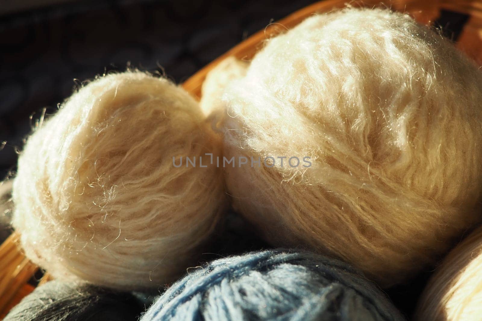 White, beige and blue woolen and acrylic threads wound into a ball or skein. Several skeins of light yarn in a basket. Knitting as a hobby. A clew of thread