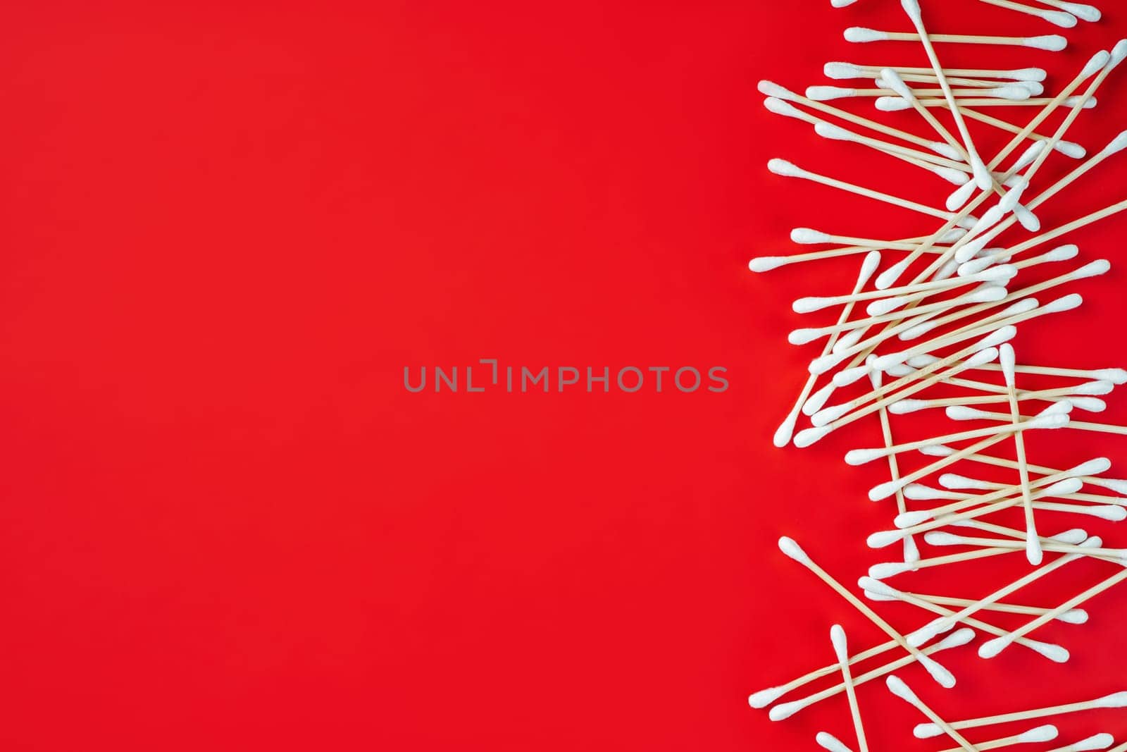 Wooden cotton buds on red background. Hygienic accessory product concept. Environmental conservation concept. Auricle hygiene. Beauty concept. Top view. Flat lay.